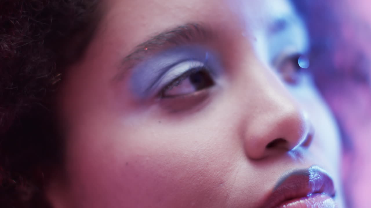 Biracial woman with dark curly hair in blue and pink light, slow motion