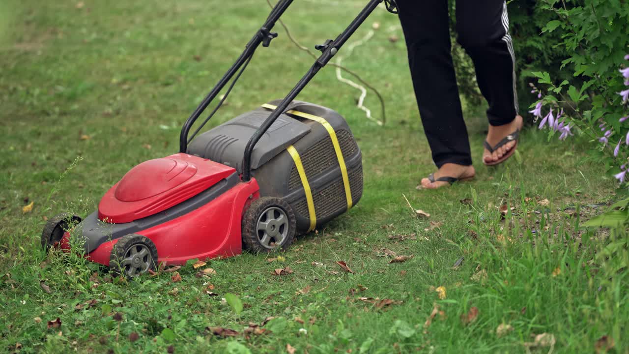 woman cutting grass in his yard with corded electric lawn mower.