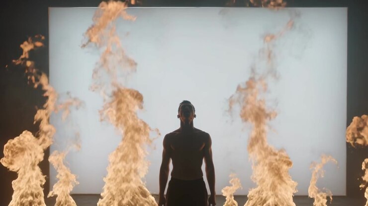 Igniting fire columns framing shirtless man in dark pants on dark stage, back panel emitting smoke