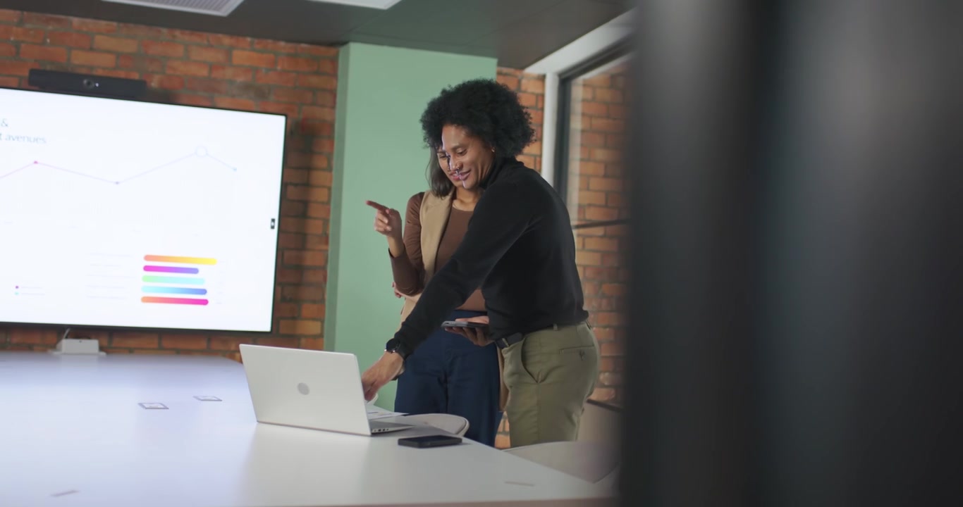 African American coworkers in blazer reviewing wall chart pointing laptop man holding phone smiling