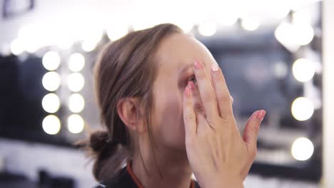 Makeup-artist-applies-foundation-of-a-beautiful-young-girl-in-the-makeup-studio-using-fingers-and-brush.-Close-up