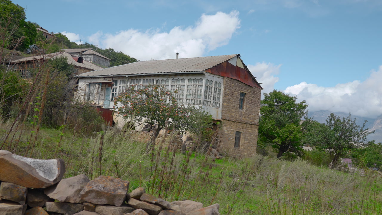 Old Stone House On Hillside With Glassed Veranda And Overgrown Meadow, Stacked Stone Wall In Foreground