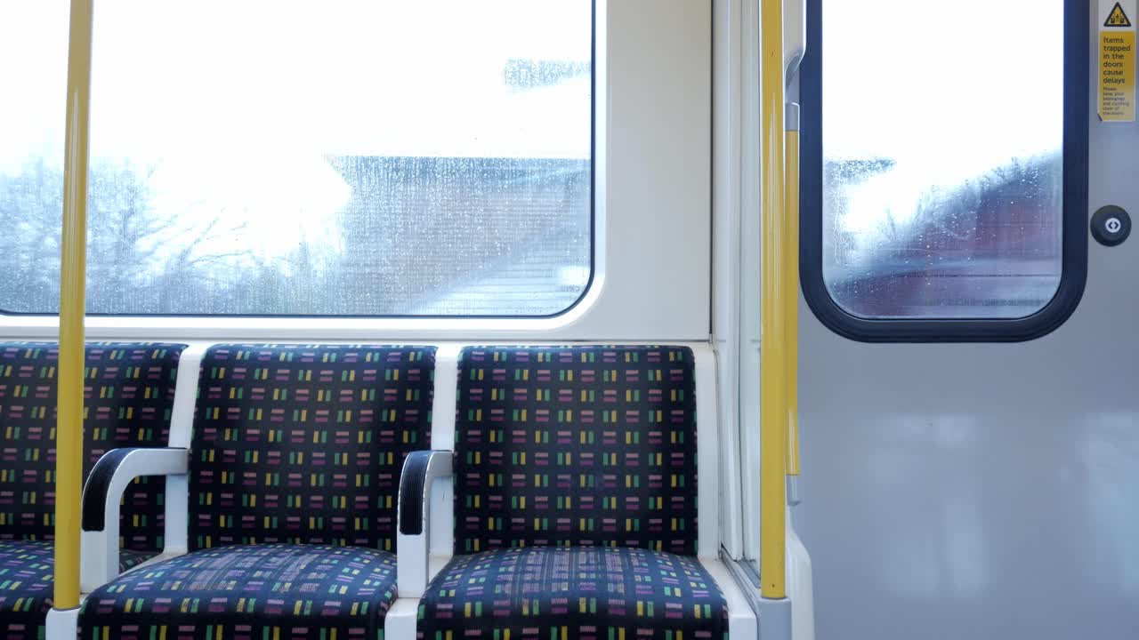 A London Tube interior with patterned seats and bright yellow poles on a rainy day