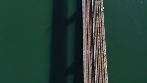 An-aerial-shot-over-train-tracks-over-a-bay-with-green-water-on-a-sunny-day