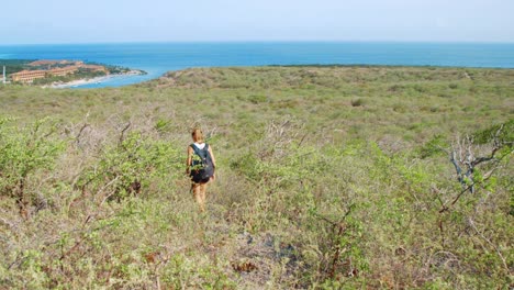 young woman hiking downhill towards caribbean sea in curacao