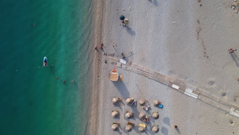 summer vacation on beautiful beaches in albania, tourists sunbathe under umbrellas near turquoise seawater