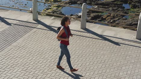 mujer afroamericana con mochila y caminando por el paseo marítimo