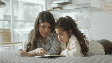 mom and little daughter drawing on digital tablet together at home