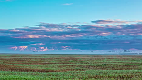 Timelapse-De-Toma-Amplia-De-Una-Enorme-Llanura-Cubierta-De-Hierba-Sobre-La-Que-Flotan-Nubes-Oscuras-Bajo-Un-Cielo-Azul