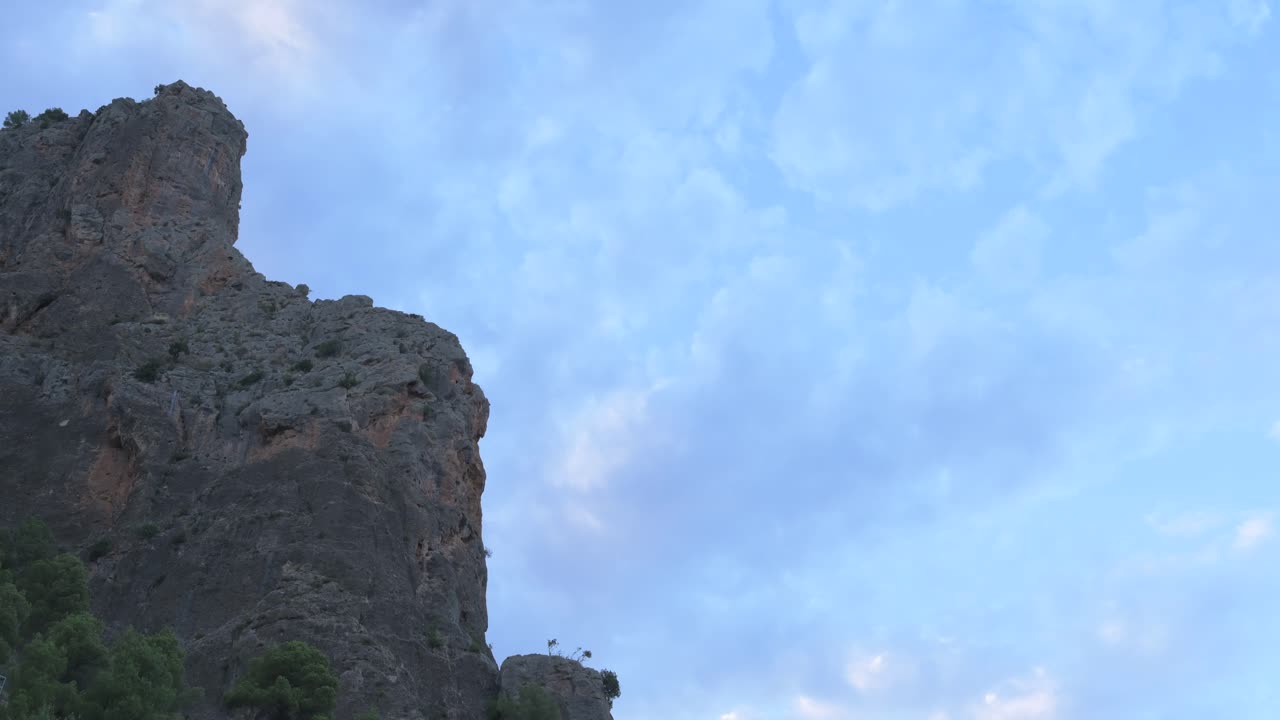 A captivating timelapse shows clouds gracefully moving over a rugged mountain peak against a blue sky