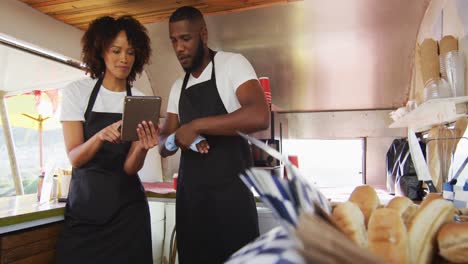 african american couple wearing aprons smiling while using digital tablet in the food truck