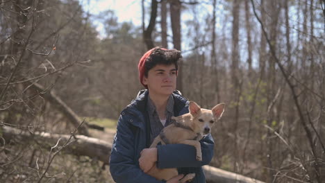 Mujer-Joven-Con-El-Pelo-Corto-Da-Un-Paseo-Por-El-Bosque-Sosteniendo-Un-Perro-Pequeño-1