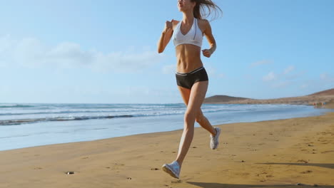 Beautiful-woman-in-sports-shorts-and-t-shirt-running-on-the-beach-with-white-sand-and-blue-ocean-water-on-the-island-in-slow-motion.-Waves-and-sand-hills-on-the-back-won