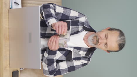 Vertical-video-of-Old-man-looking-at-laptop-counting-money.