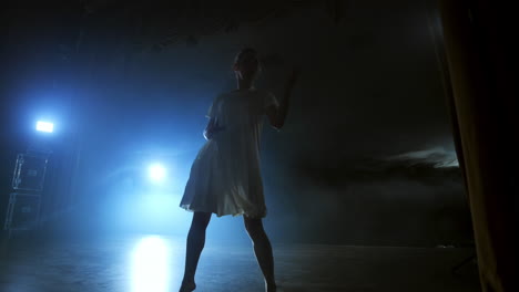 a dramatic scene of modern ballet a lone ballerina in a white dress performs dance steps using modern choreography.