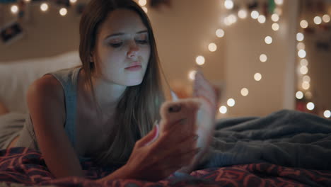 Hermosa-Adolescente-Acostada-En-La-Cama-Enviando-Mensajes-De-Texto-Usando-Un-Teléfono-Inteligente-Navegando-Por-Las-Redes-Sociales-Chat-En-Línea-Disfrutando-De-Una-Noche-Relajándose-En-Casa