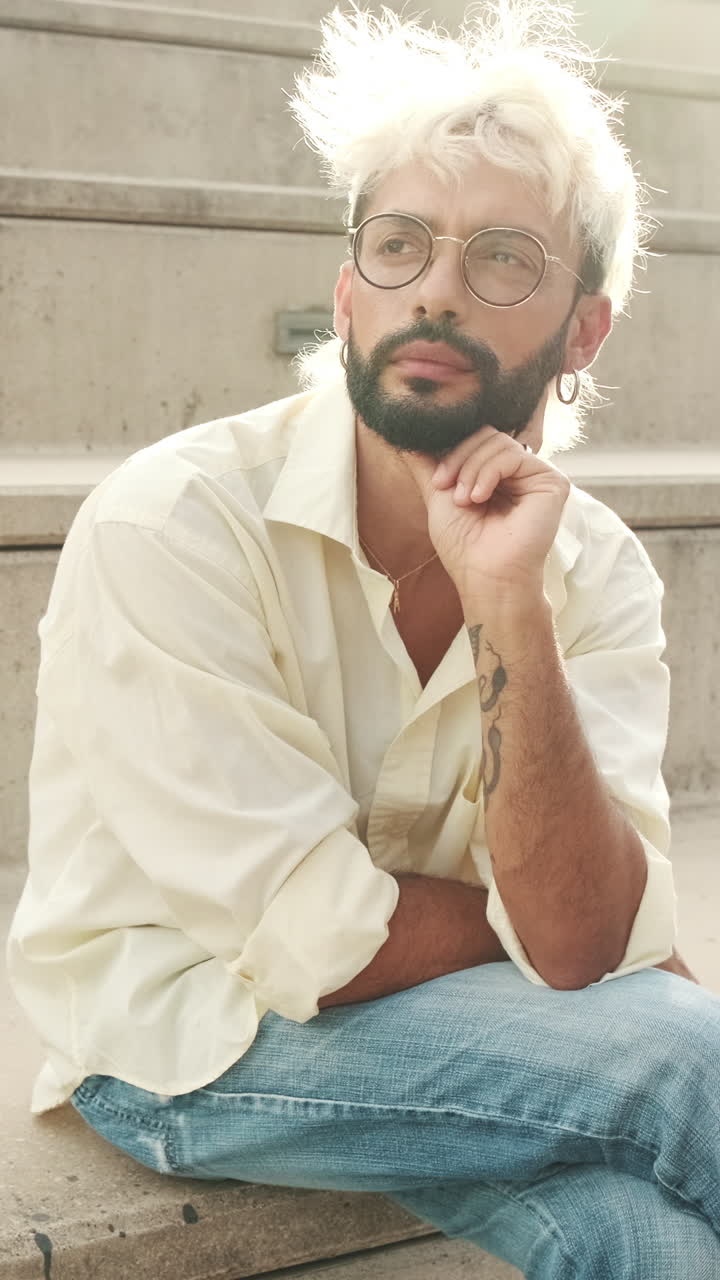 Thoughtful Young Man with Bleached Hair and Beard Sitting Outdoors