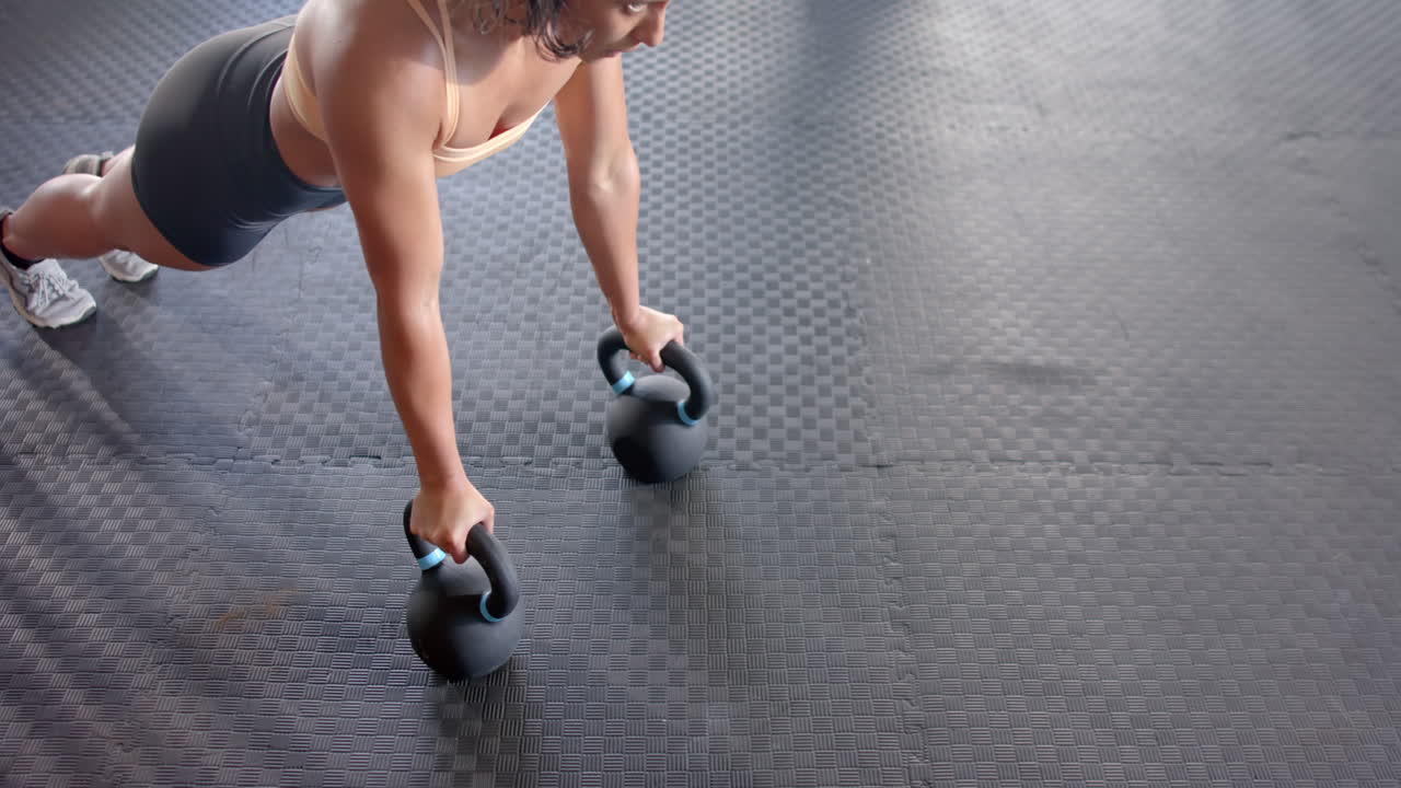 Performing push-ups with kettlebell, woman exercising in gym for fitness training, copy space
