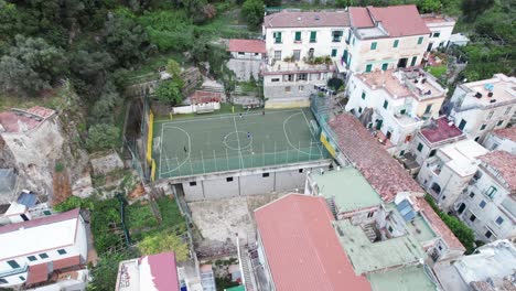 an aerial shot circling a rooftop soccer or football pitch as kids train in the cliffs of amalfi town, one of the most popular tourist destinations on the famous amalfi coast in italy