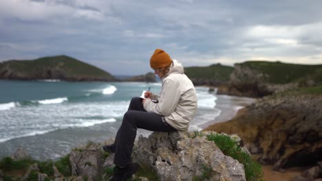 tagebuchschreiber schreibt ein notizbuch an einer klippe mit wellen, die am strand abstürzen