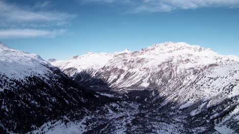 Vista-Aérea-De-Un-Valle-Cubierto-De-Nieve,-Montaña-Y-Bosque-En-Un-Soleado-Día-De-Invierno-En-Suiza