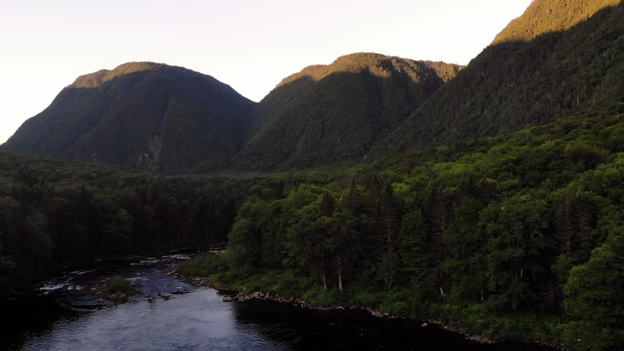 disparo de un dron elevándose sobre un río, 3 montañas al fondo
