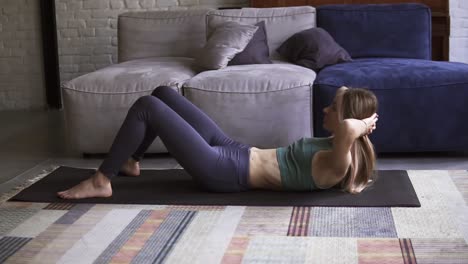 Sporty-woman-is-doing-abs-exercises-crunches-on-floor-on-mat-at-home