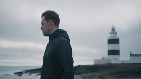 Man-standing-in-front-of-a-lighthouse-and-looking-into-the-distance