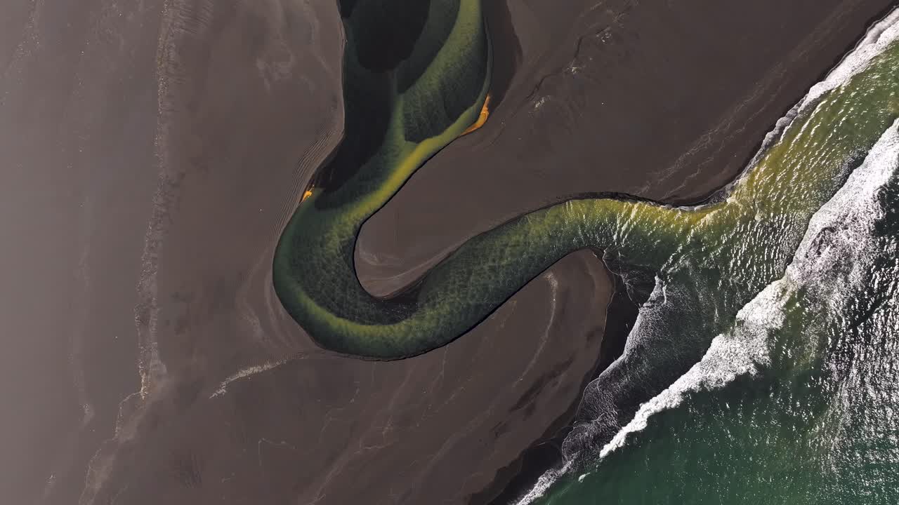 Volcanic River flowing into Atlantic Ocean with crashing waves. Sunny summer day on Iceland island. Aerial top down shot
