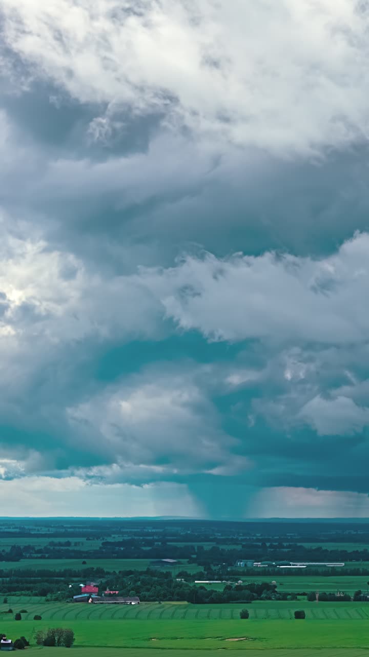Nuvole temporalesche scure si addensano sopra un vasto paesaggio agricolo, ripresa aerea verticale.