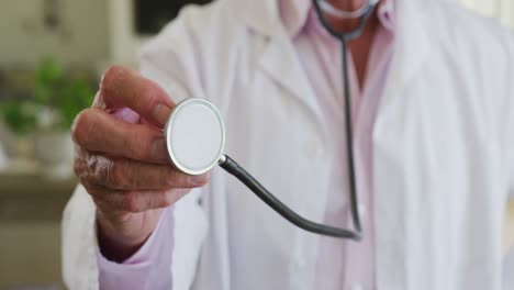 mid section of caucasian senior male doctor holding stethoscope at home