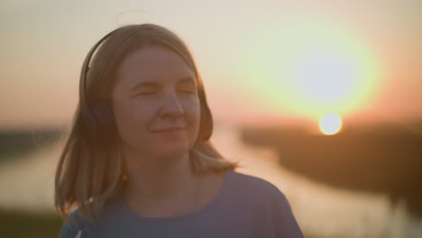 close-up of a woman wearing a headset, smiling contentedly while bathed in the warm glow of the setting sun. the sun's rays create a soft, golden effect around her, adding a peaceful ambiance