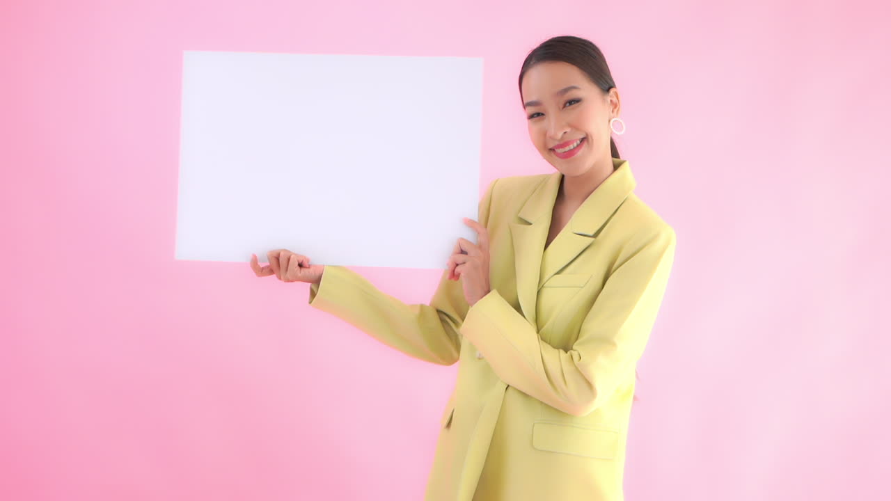 핑크 스튜디오 배경에 행복한 얼굴 표정으로 종이 포스터 배너의 빈 시트를 들고 아시아 사업가