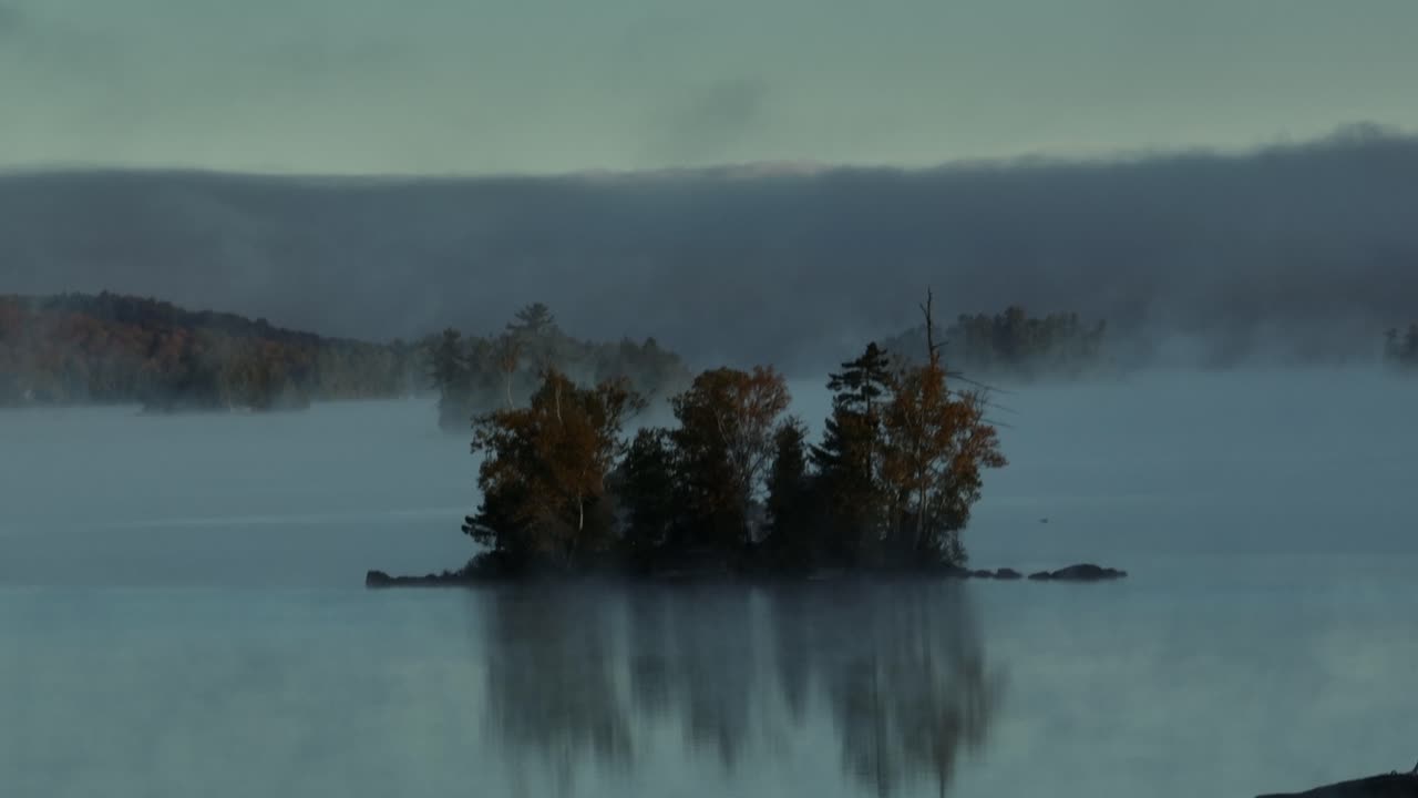 Aerial flight towards island on lake surrounded by fog