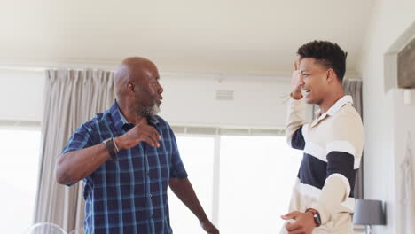 Excited-african-american-father-and-adult-son-cheering-at-sport-on-tv-and-high-fiving,-slow-motion