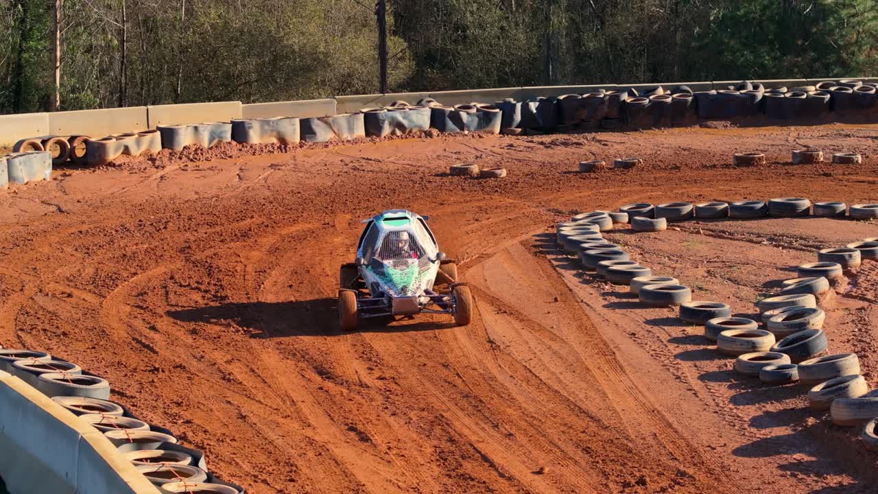 Buggy da corsa fuoristrada che derapa su una pista sterrata con file e pile di pneumatici - ripresa aerea