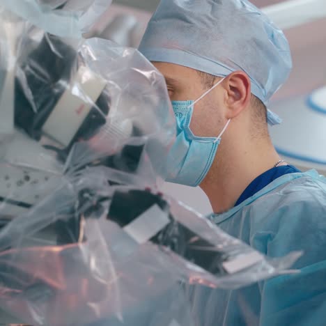 neurosurgery. side view of focused doctor in medical mask and uniform looking into the modern microscope during the surgery. healthcare concept.