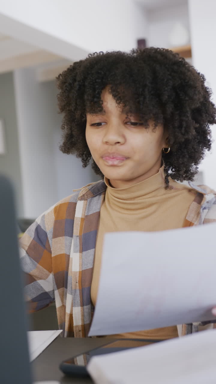 Vertical video of african american teenager girl with documents using laptop, slow motion