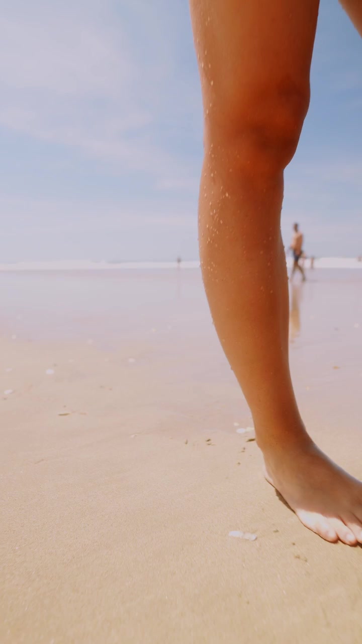 Primo piano di gambe scalze che camminano su una spiaggia di sabbia soleggiata