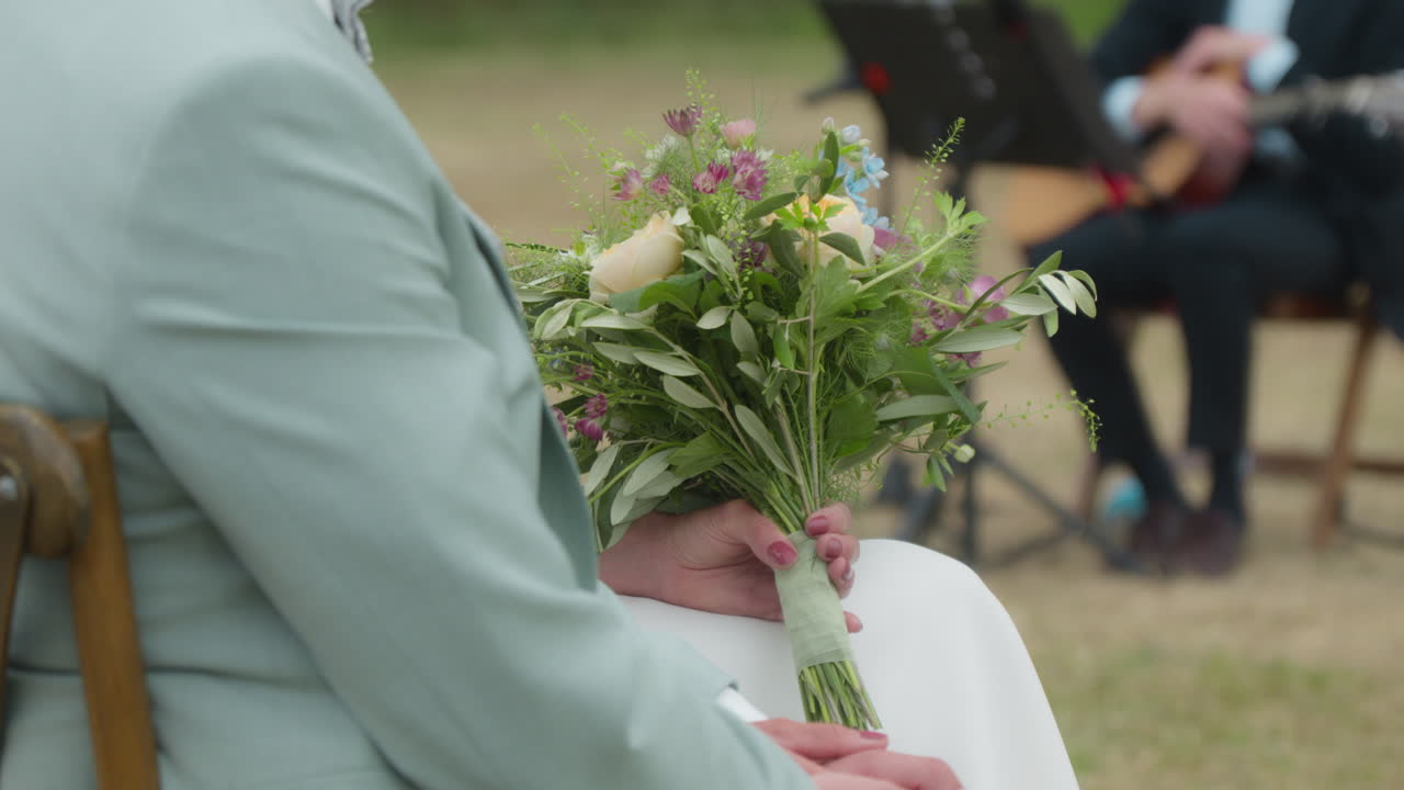 Bride clutching bouquet at outdoor wedding ceremony. Intimate and serene scene, ideal for romantic event promotions