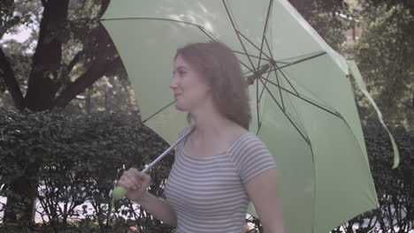 millennial woman walks along a hedgerow carrying a neon green umbrella