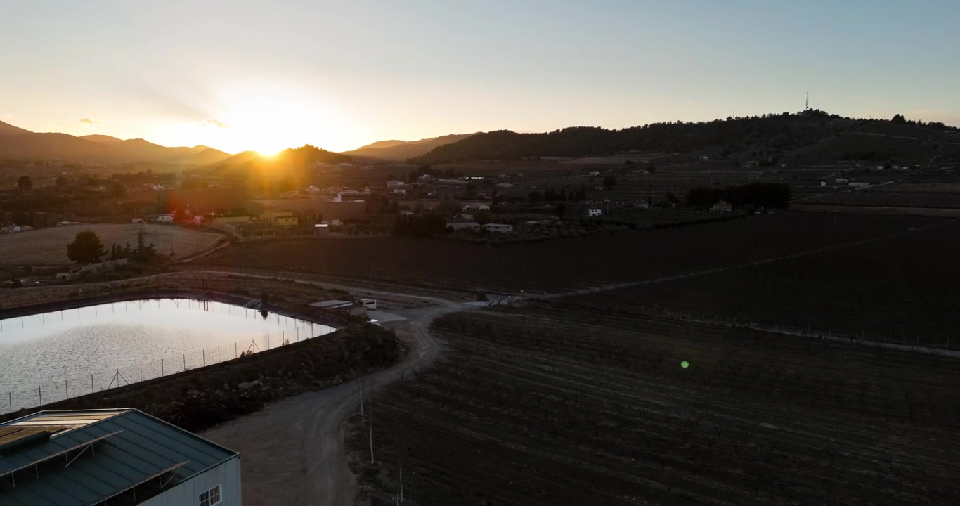 Ripresa aerea con drone su uno stagno riflettente e terreni agricoli rurali durante un tramonto dorato vicino a Bullas, Murcia, Spagna.