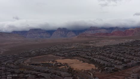 Aerial-wide-descending-shot-of-Red-Rock-Canyon-with-desert-suburbs-in-the-foreground-in-Las-Vegas,-Nevada