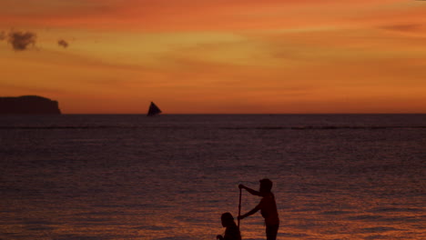 artistic reveal shot of two people on paddle boat while in silhouette of sunset
