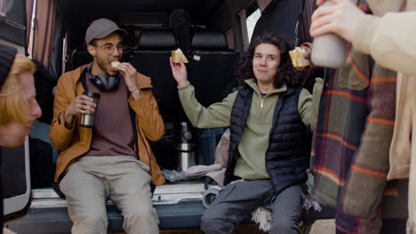 a movie production team taking a break while eating a sandwich and talking behind a van in the street