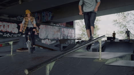 teenagers friends riding together on scooter and bike at city skatepark.