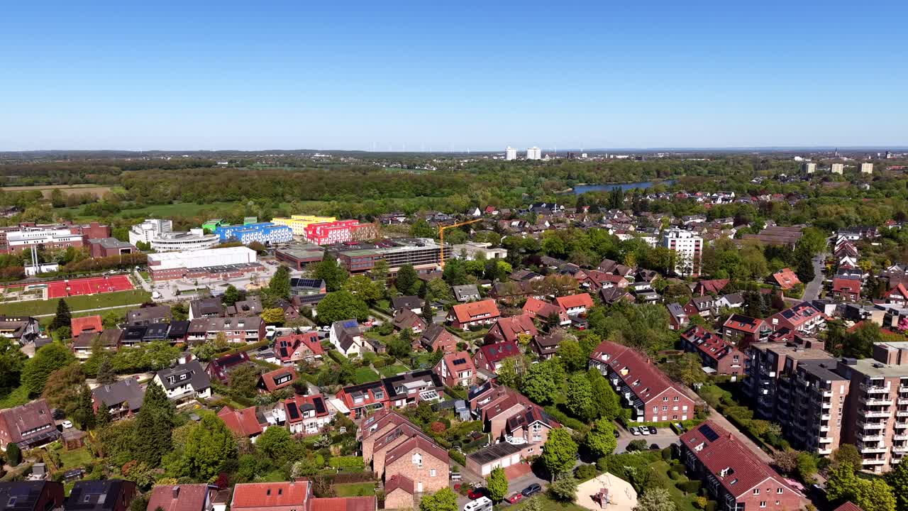 Szerokie ujęcie z lotu ptaka niemieckiej dzielnicy mieszkalnej z domami z czerwonej cegły, kolorowymi budynkami mieszkalnymi i kwitnącymi wiosennymi drzewami pod słonecznym niebem w spokojnej europejskiej scenerii podmiejskiej.