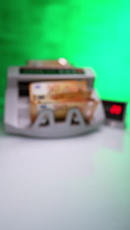 Placing cash into money counting machine. Fifty euro bills counted in device and male hand puts them on the desk. Vertical video.