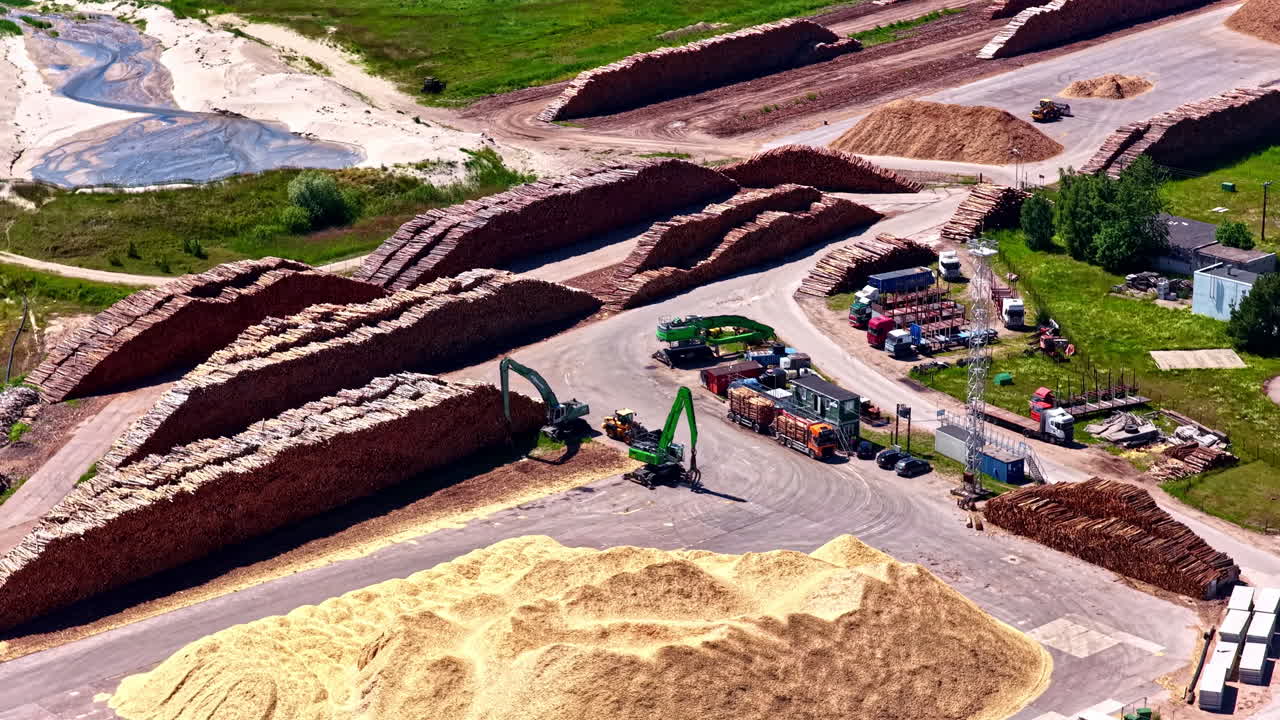 Aerial parallax view of timber stacks, sawdust piles, and forestry machinery operating at Mērsrags Port, Latvia