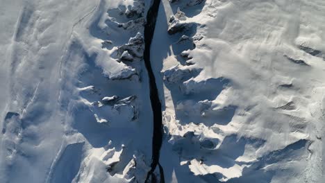 aerial top view over a glacier river flowing through a snow capped canyon, on a sunny day